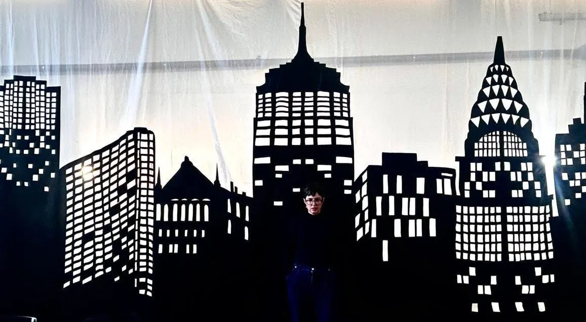 A person standing in front of a black silhouette of buildings Description automatically generated